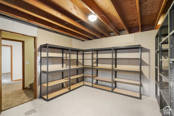 Unfinished basement space featuring exposed wood joists and multiple metal shelving units