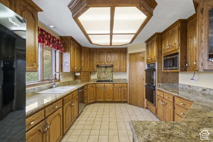 Kitchen featuring wood cabinetry, stone countertops, double wall ovens, a built-in microwave, and tile flooring