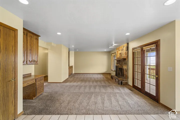 Recessed lighting illuminates this space featuring a stone-clad fireplace and wood-frame French doors