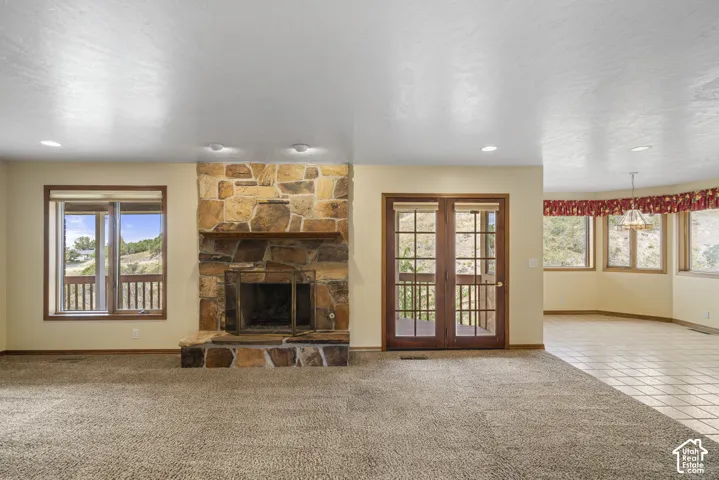 Stone-faced fireplace with a hearth, double French doors, large windows, recessed lighting, and tile flooring