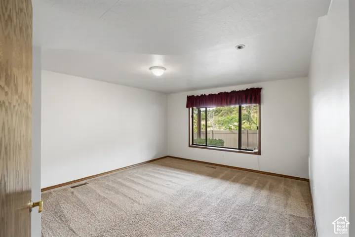 Carpeted room with white walls, a large window, wood-finish trim, and a flush mount light fixture