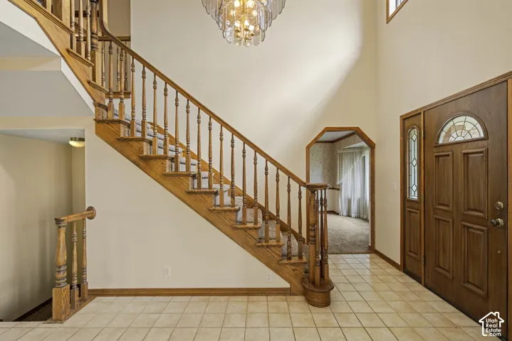 Two-story entryway featuring a wood staircase with carpeted treads, a crystal chandelier, an arched doorway, and a wood entry door with decorative glass