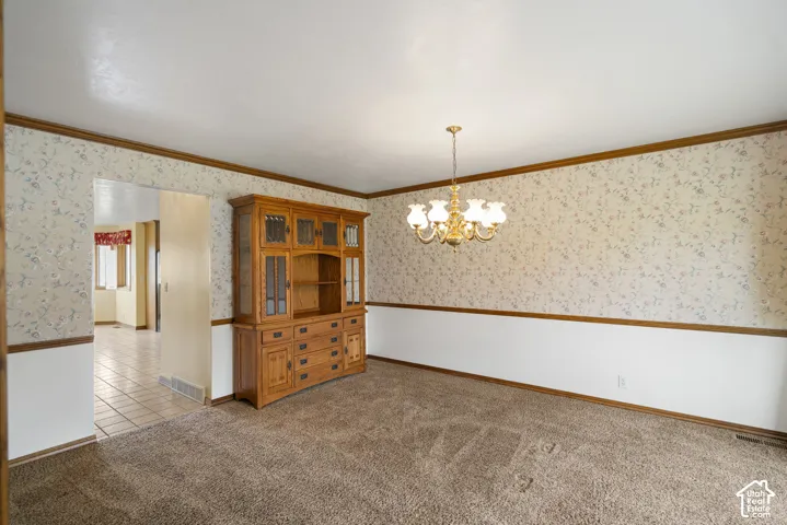 Carpeted room featuring a gold-toned chandelier, patterned wallpaper with chair rail, and an archway opening