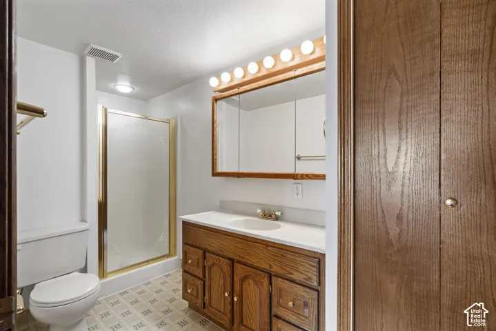 Bathroom featuring a single vanity with wood cabinetry, a mirrored medicine cabinet, a shower with a gold-toned frame, and patterned tile flooring