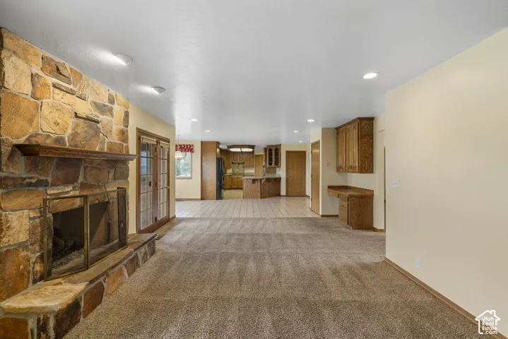 Stone-clad fireplace with a wood mantel, glass double doors, recessed lighting, built-in desk, and wood cabinetry