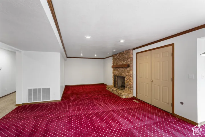 Spacious room featuring red patterned carpeting, a stone-clad fireplace with a wood mantle, and recessed lighting