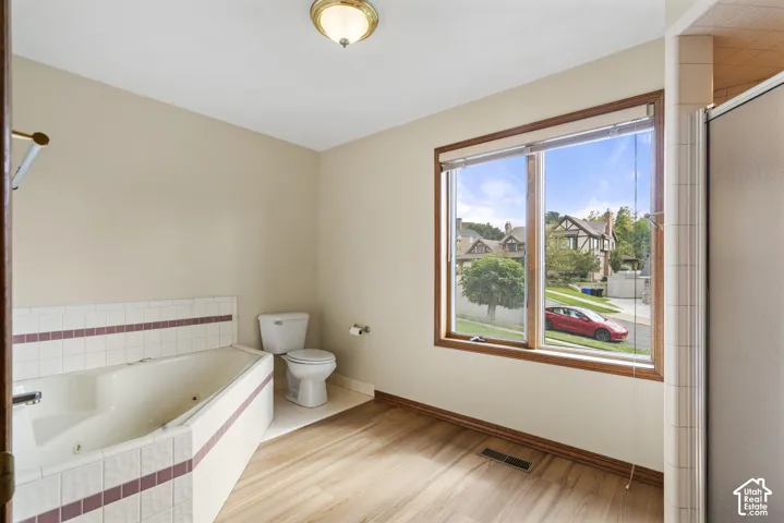 Primary bathroom with jetted soaking tub with tile surround, wood-finish flooring, and a large window