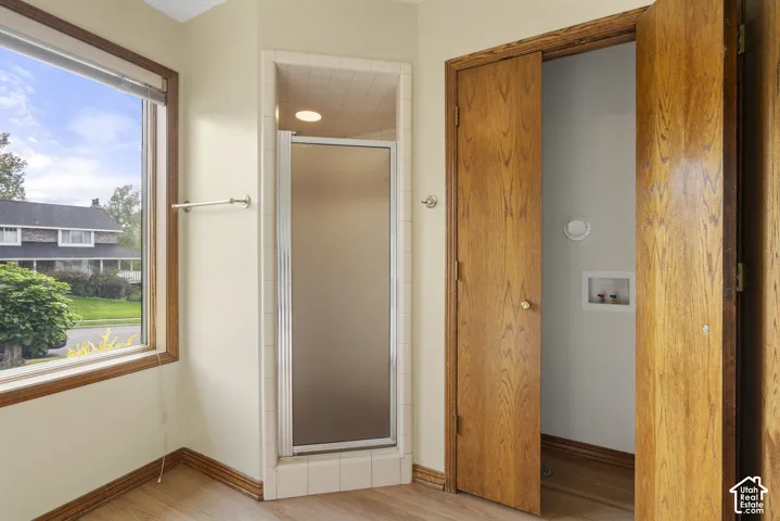 Wood-finish flooring with a large window, a glass-enclosed shower, and wood bi-fold doors