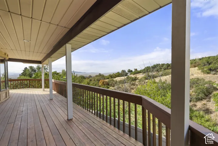 Expansive covered deck with wood flooring and a wood railing, offering open-air scenery