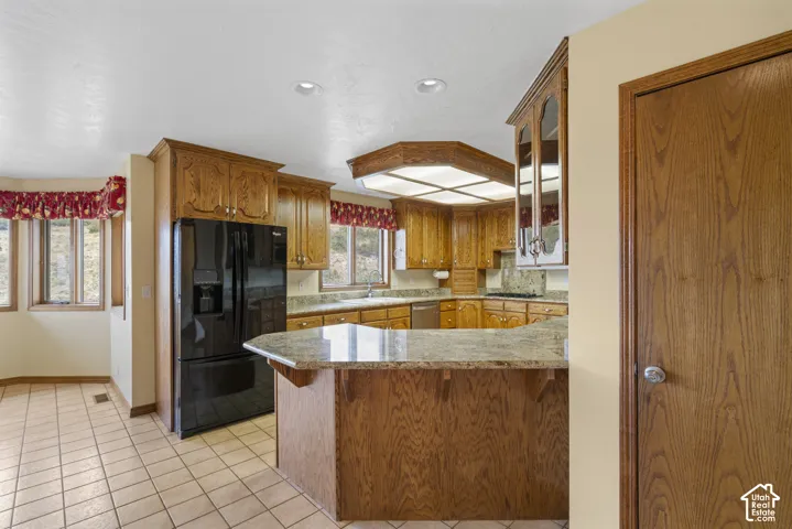 Kitchen featuring wood cabinetry, a built-in black refrigerator, a kitchen island with a stone countertop, a tile backsplash, and recessed lighting