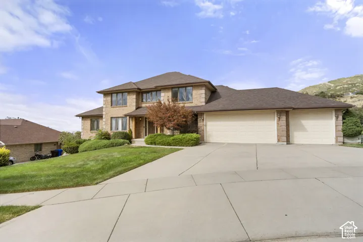 Brick and stone exterior with multiple windows, an attached multi-car garage, and a concrete driveway