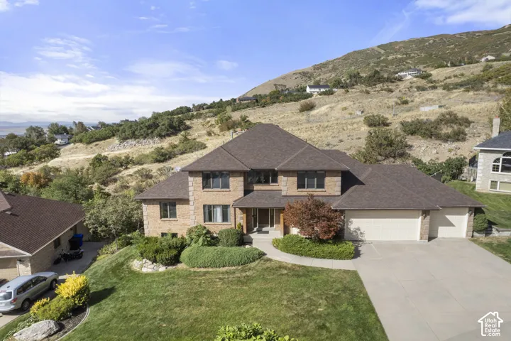 Elegant two-story residence featuring a brick and stone exterior with a dark asphalt shingle roof, multiple windows with dark trim, and a three-car garage