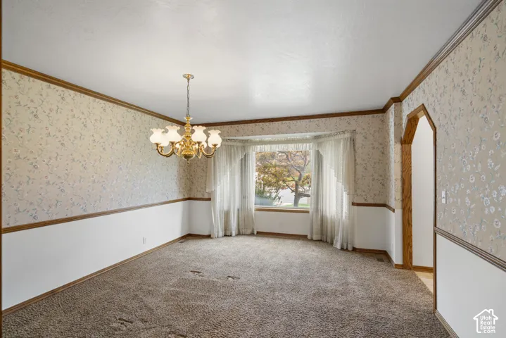 Room featuring a bay window, patterned wallpaper, a brass chandelier, and an arched doorway