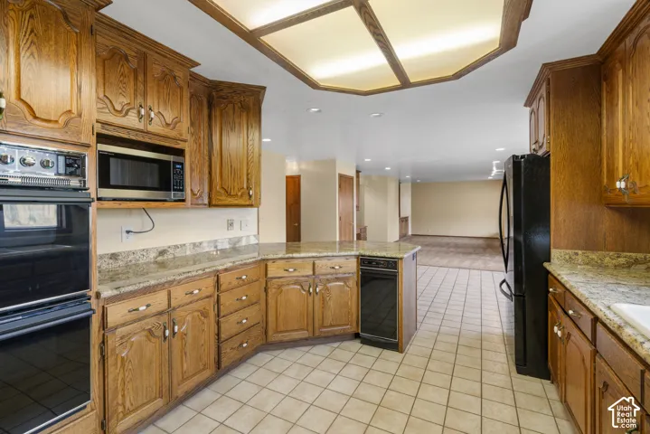 Kitchen featuring wood cabinetry, light-toned countertops, tile flooring, and integrated black appliances