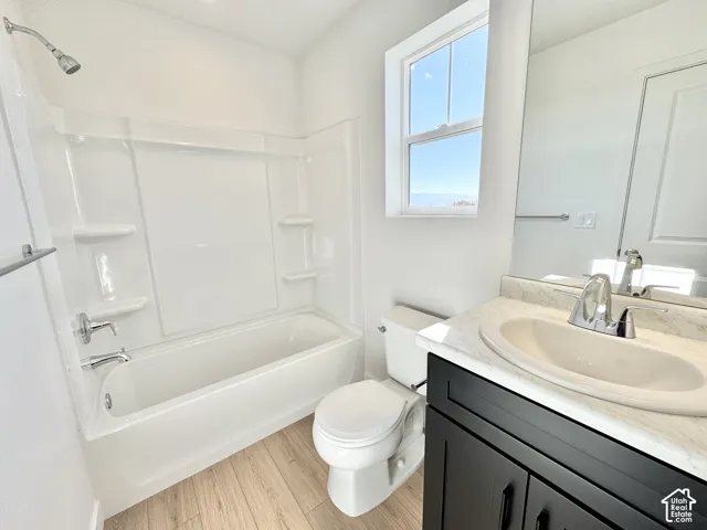 Bathroom featuring a white bathtub, wood-finish flooring, a single window, a dark wood-finish vanity, and a light-colored countertop