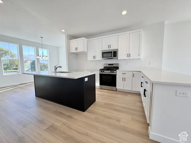 White shaker cabinetry, stainless steel appliances, light wood-finish flooring, a kitchen island with seating, and recessed lighting
