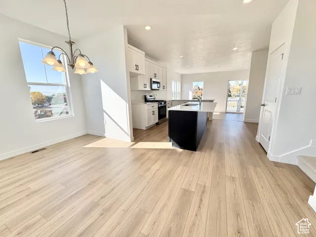Open-concept living area featuring wood-finish flooring, a contemporary kitchen with white cabinetry and a dark island, and a dining area with a chandelier