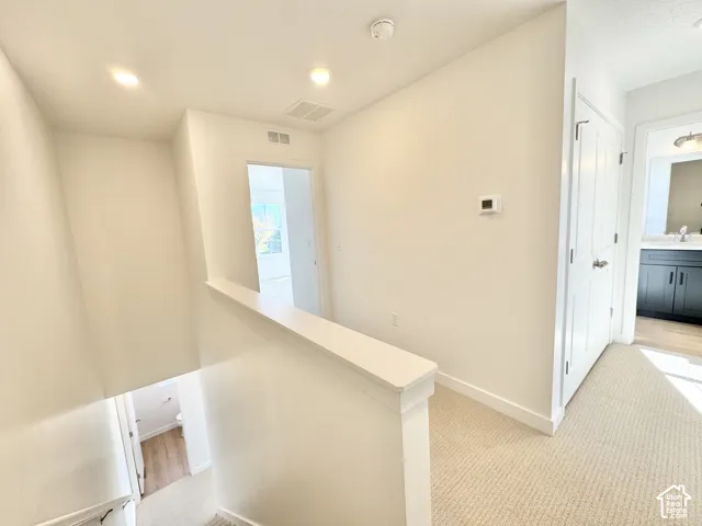 Carpeted hallway with white walls, recessed lighting, and a white railing