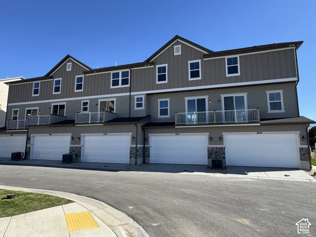 Multi-story townhome exterior featuring an attached garage, white garage doors, upper-level balconies with white railings, and a combination of stucco and board and batten siding