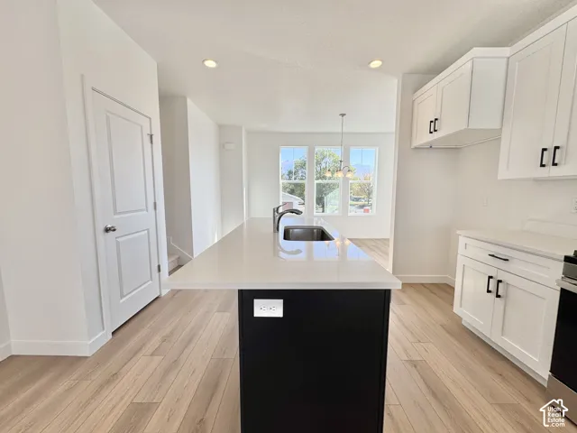 Kitchen featuring wood-finish flooring, white cabinetry with black hardware, an island with an integrated sink, and recessed lighting