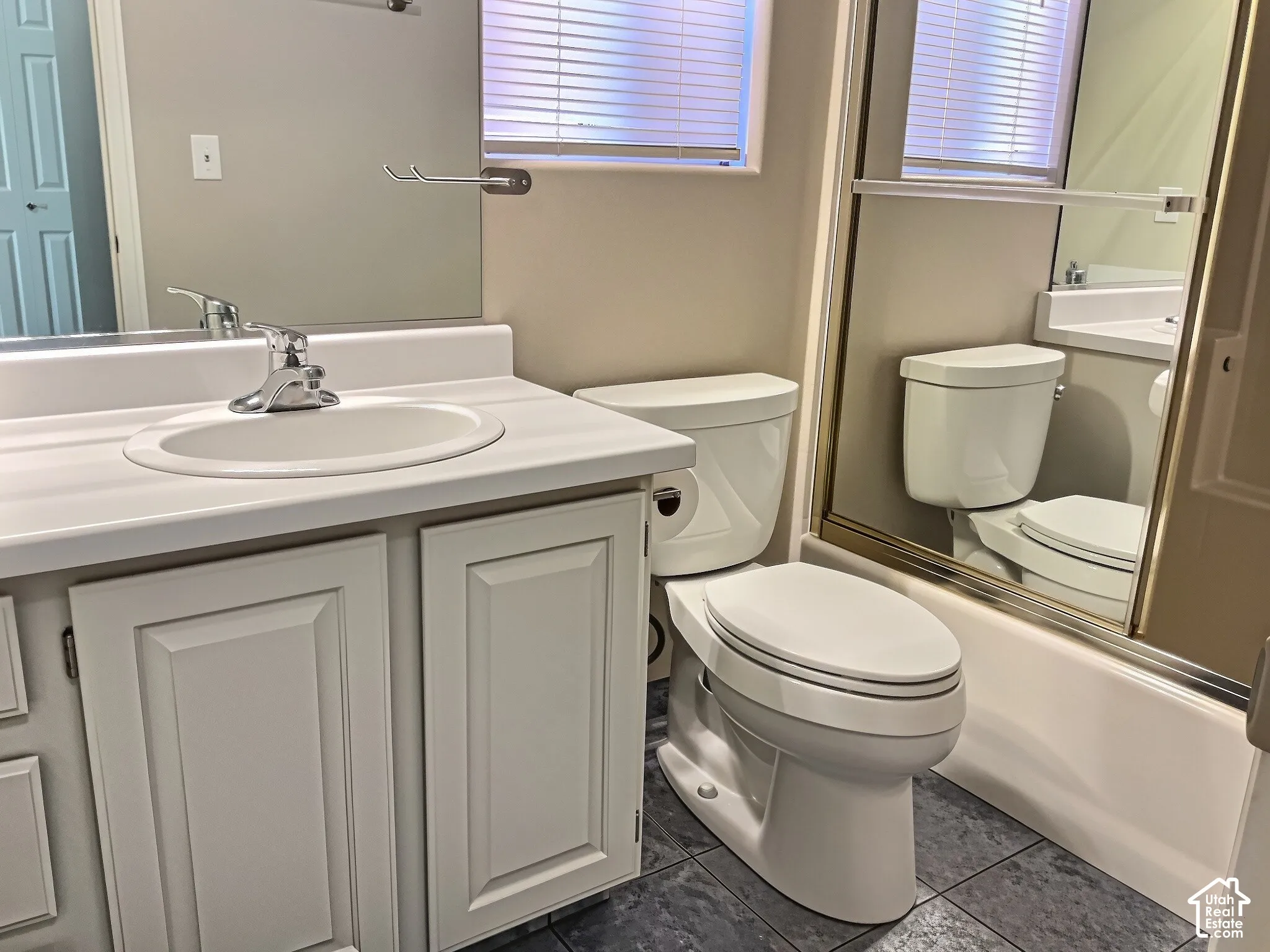 Vanity with a white countertop and integrated sink, chrome faucet, white paneled cabinetry, and a toilet with a mirror above
