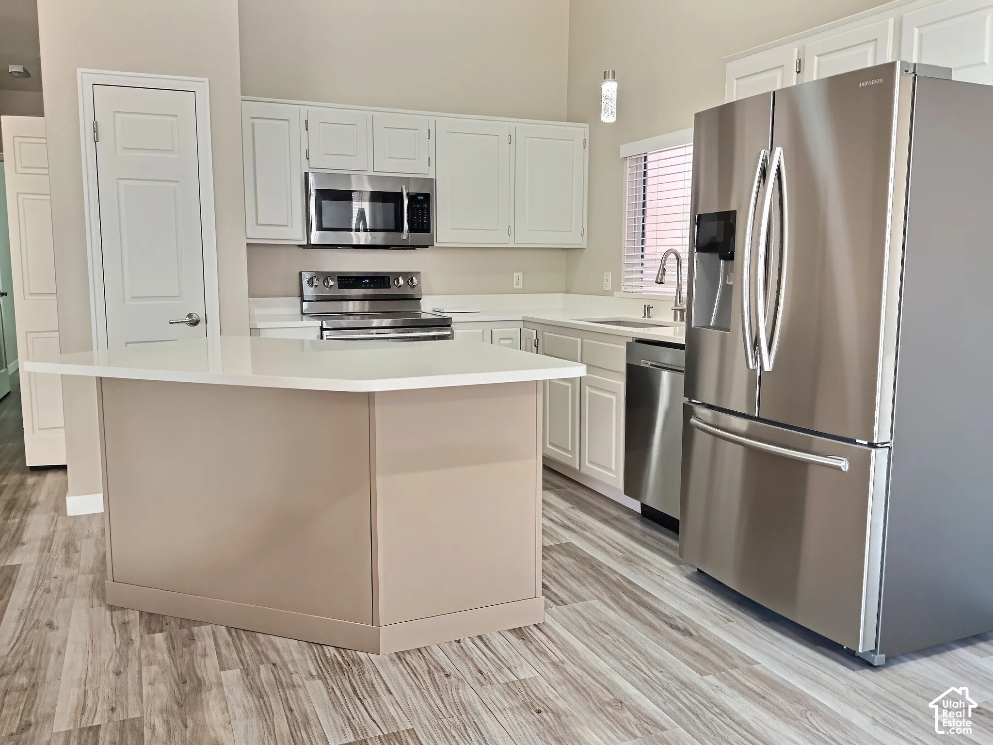 Kitchen with white cabinetry, stainless steel appliances, a center island with a light-toned base, and wood-finish flooring