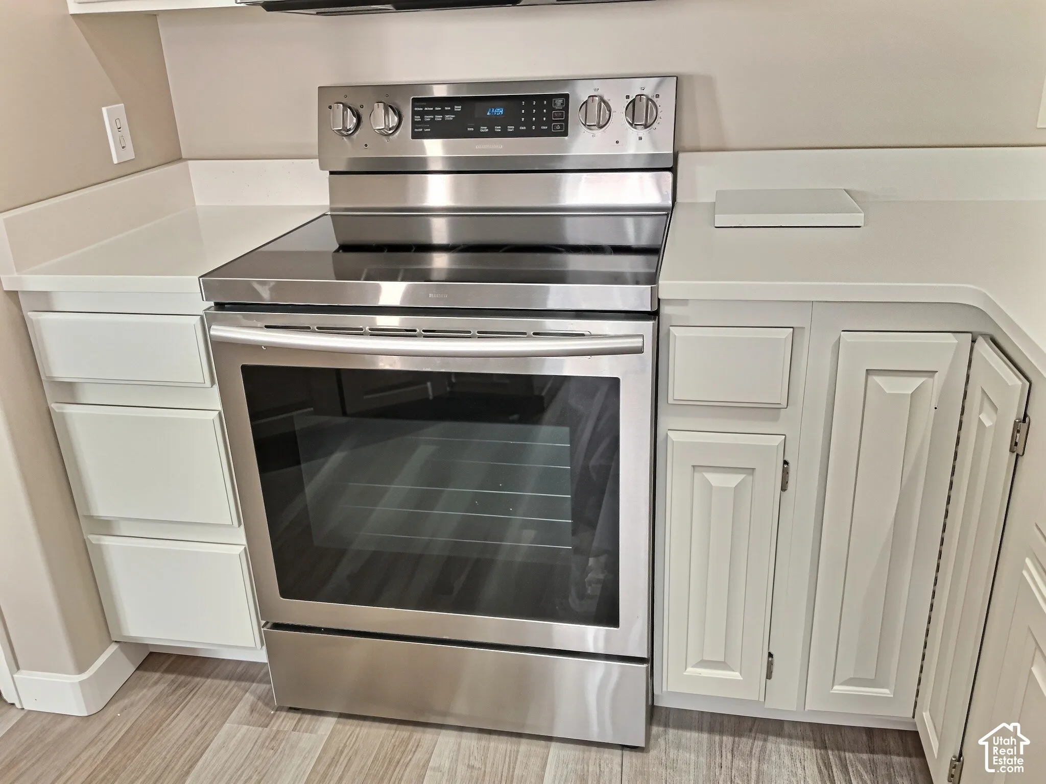 Stainless steel electric range with a smooth cooktop, white countertops, white cabinetry, and wood-finish flooring