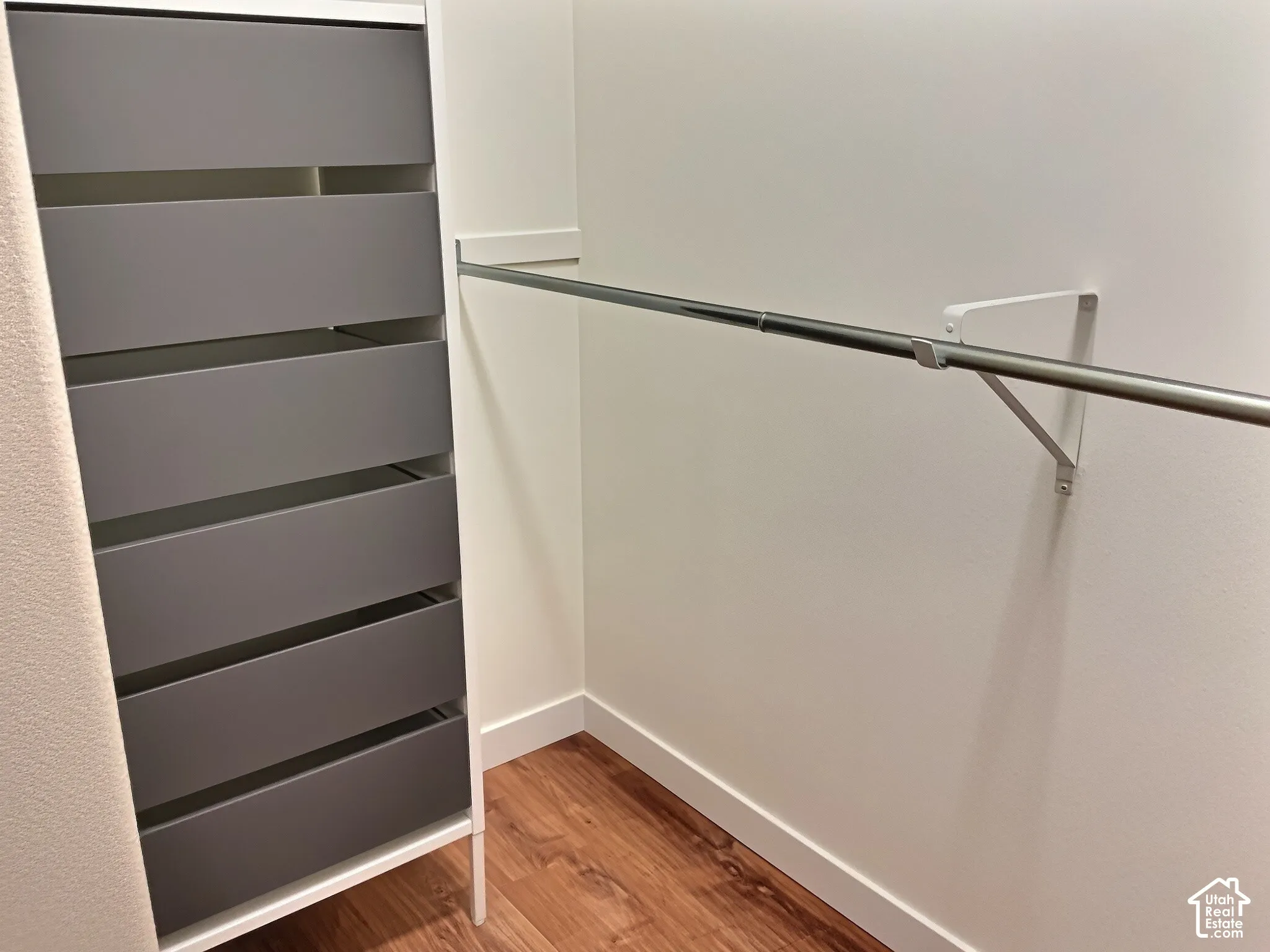 Built-in closet system with six drawers, mounted hanging rod, and wood-finish flooring