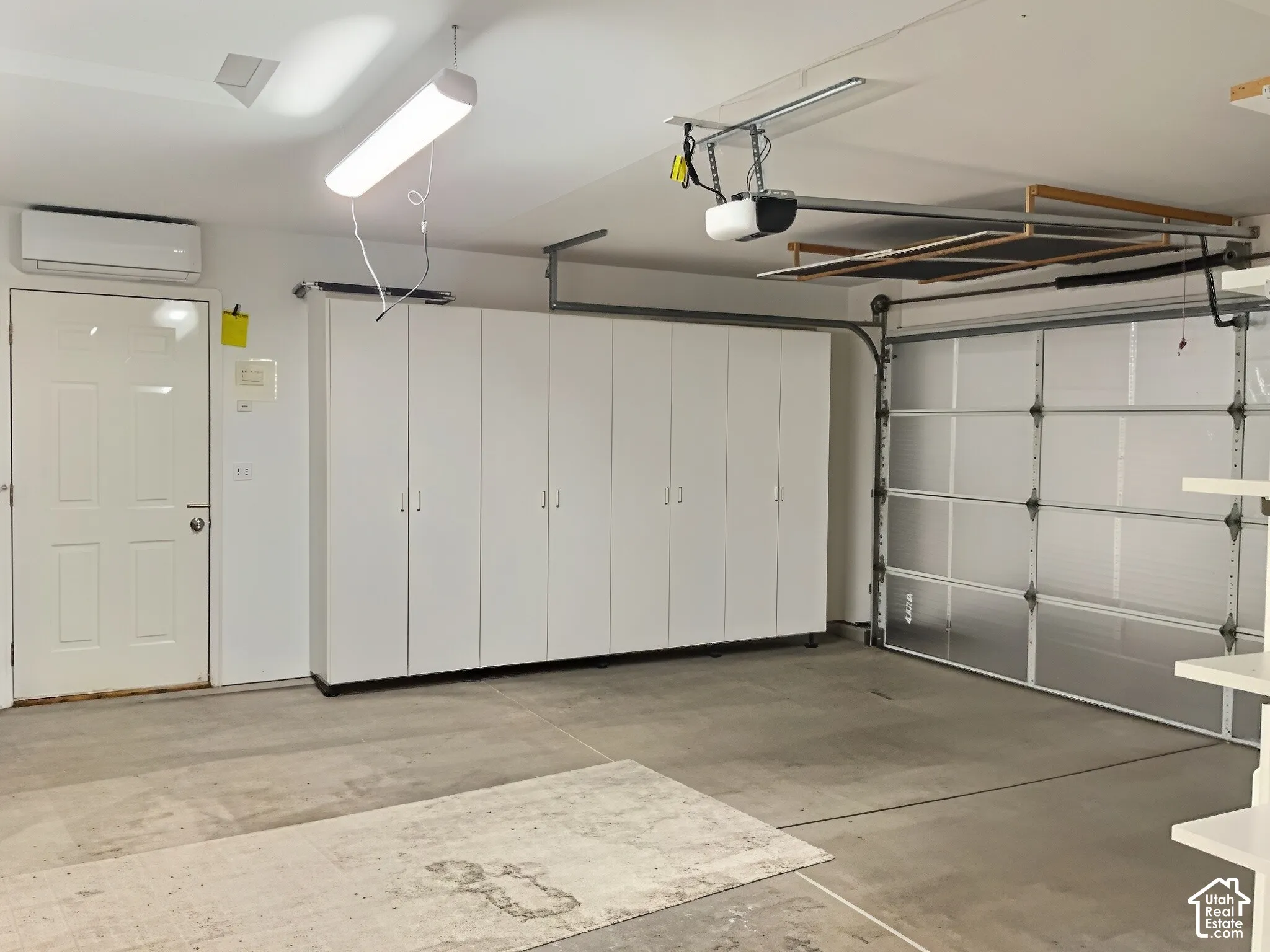 Spacious garage featuring epoxy-coated concrete flooring, white panel cabinetry with ample storage, dual garage doors with windows, integrated ceiling-mounted lighting, and direct interior access via white panel door