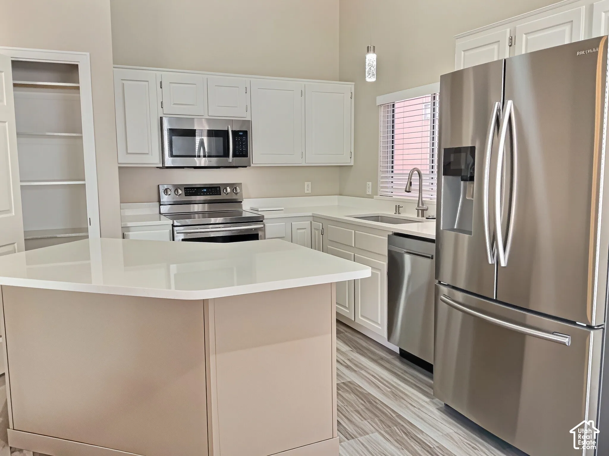 Kitchen featuring white cabinetry, stainless steel appliances, light-toned countertops, a central island, and wood-finish flooring