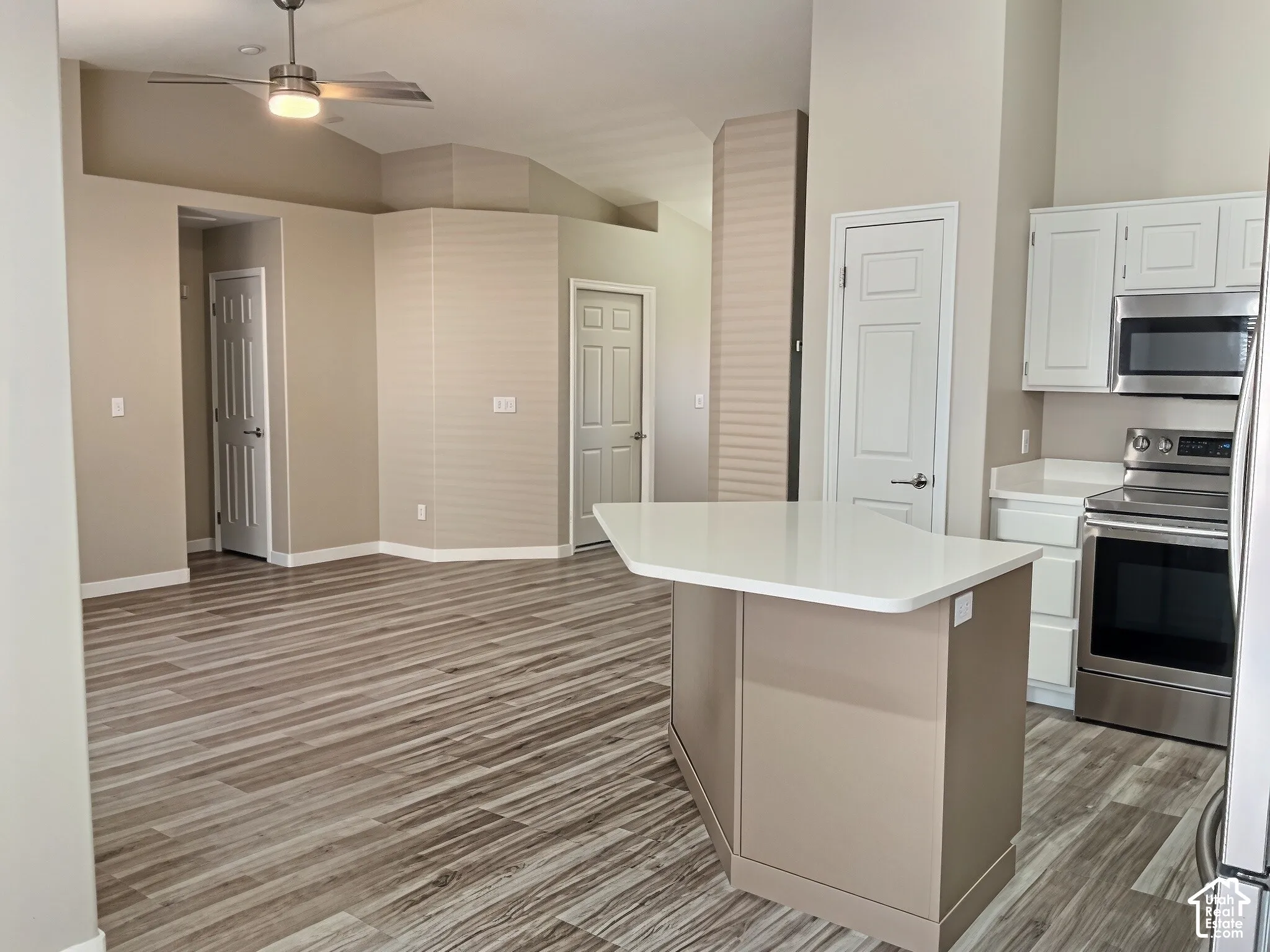 Open-concept kitchen and living area featuring a large island with white quartz countertop, stainless steel appliances including built-in wall oven and microwave, wood-finish plank flooring throughout, recessed and pendant lighting, and white cabinetry wi