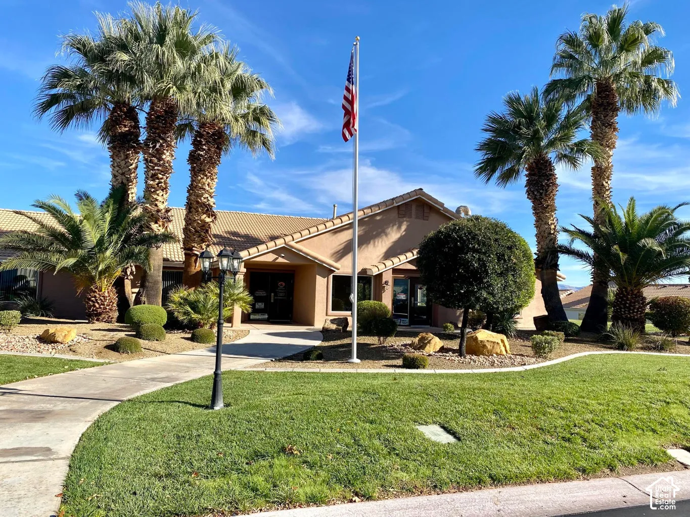 Desert-style architecture with an entry walkway, multiple mature palm trees, and landscaped grounds featuring manicured bushes and green grass