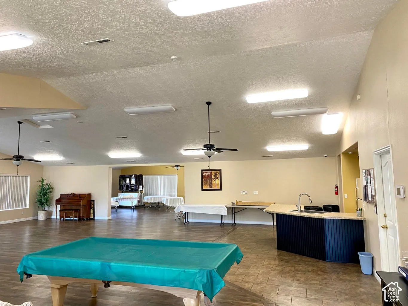 Expansive open-concept room featuring tiled flooring, recessed ceiling lighting, ceiling fans, and a built-in bar with a sink and countertop