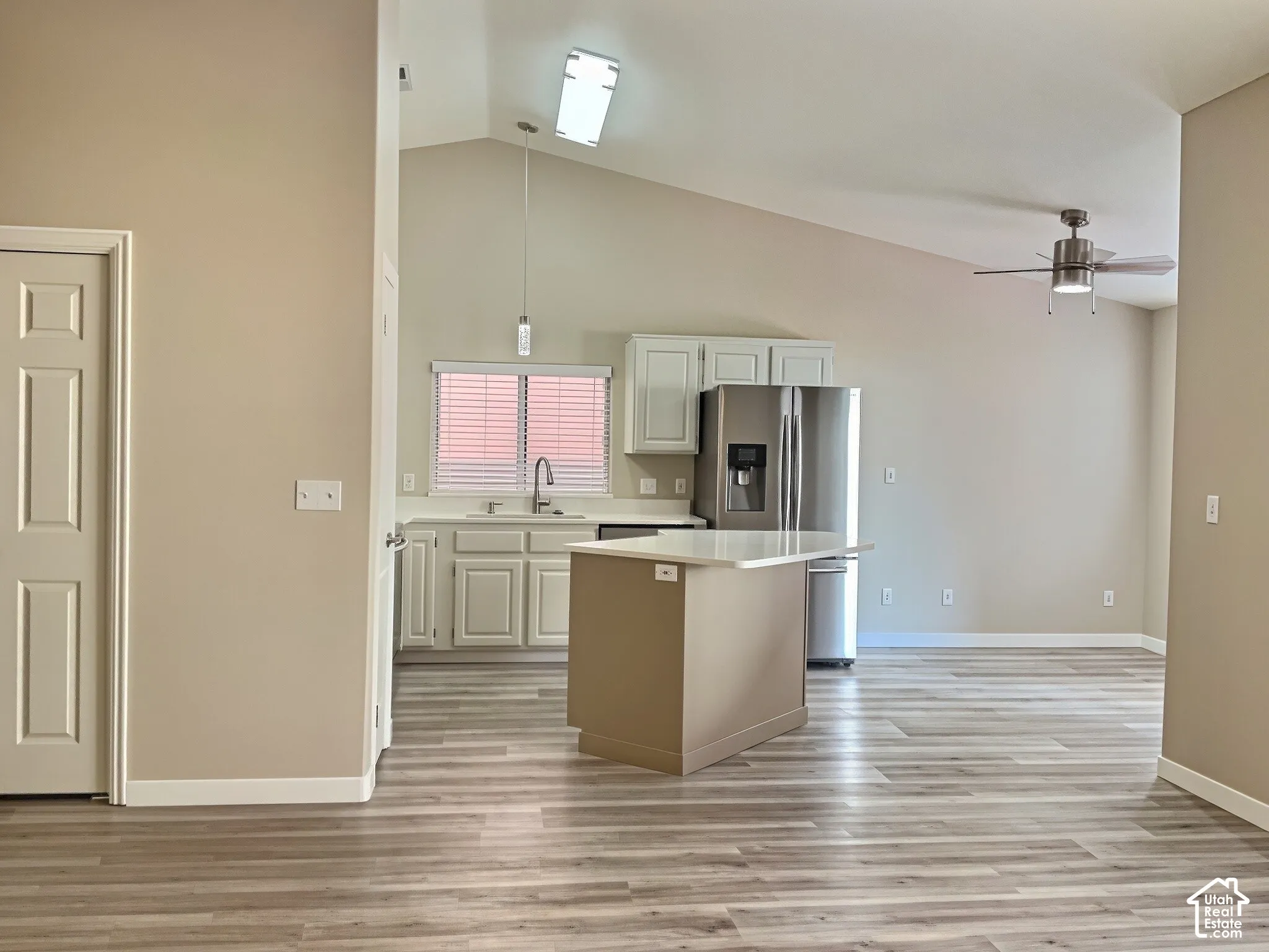 Vaulted ceilings, wood-finish flooring, white cabinetry, stainless steel appliances, and a ceiling fan