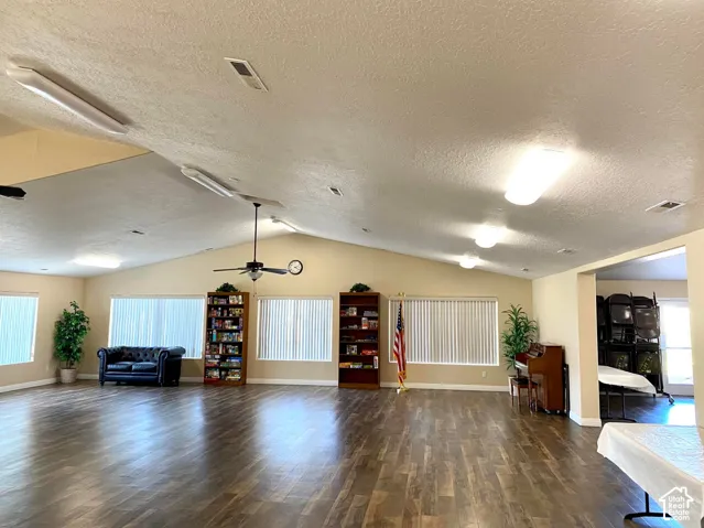 Expansive common area featuring wood-finish flooring, vaulted ceilings, and multiple windows with vertical blinds
