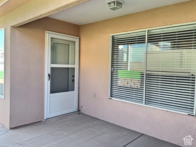 Covered patio area featuring a textured stucco finish, white frame storm door, and sliding windows with horizontal blinds