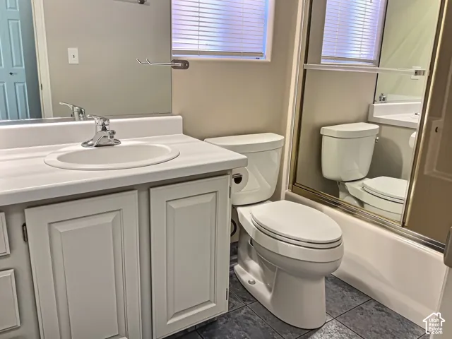 Vanity with a white countertop and integrated sink, chrome faucet, white paneled cabinetry, and a toilet with a mirror above