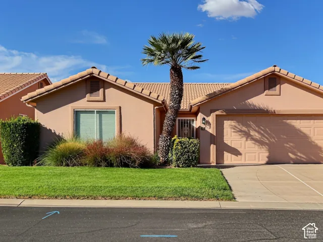 Stucco exterior with a tile roof, an integrated garage, a mature palm tree, and a manicured lawn