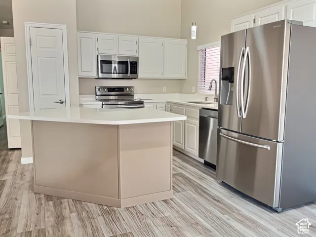 Kitchen with white cabinetry, stainless steel appliances, a center island with a light-toned base, and wood-finish flooring