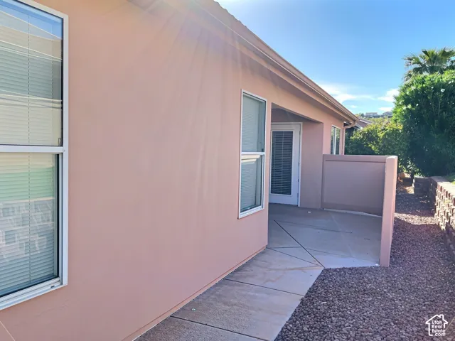 Stucco exterior with multiple windows, leading to a concrete patio area, featuring gravel landscaping and a retaining wall