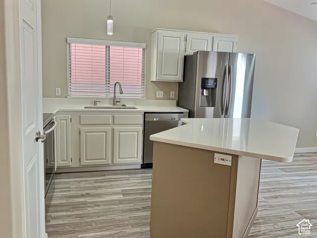 Kitchen featuring wood-finish flooring, white cabinetry, a stainless steel refrigerator, a stainless steel dishwasher, and a white countertop with a breakfast bar