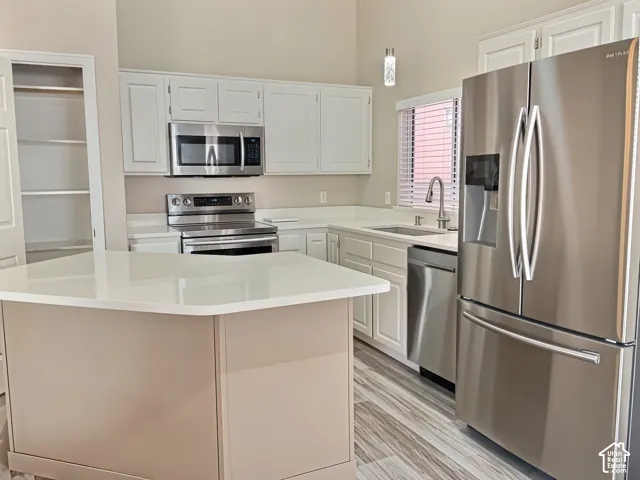 Kitchen featuring white cabinetry, stainless steel appliances, light-toned countertops, a central island, and wood-finish flooring