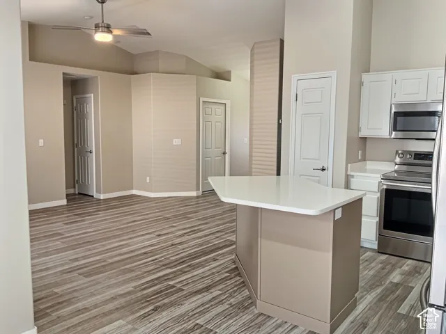 Open-concept kitchen and living area featuring a large island with white quartz countertop, stainless steel appliances including built-in wall oven and microwave, wood-finish plank flooring throughout, recessed and pendant lighting, and white cabinetry wi
