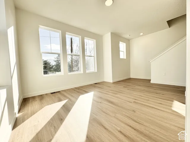 Spacious living area featuring three large windows, wood-finish flooring, recessed lighting, and a neutral color palette
