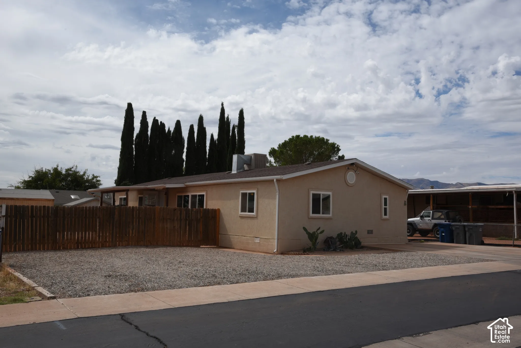 Parking Neutral-toned exterior siding, multiple windows, gravel landscaping, wood fence, and a covered parking structure