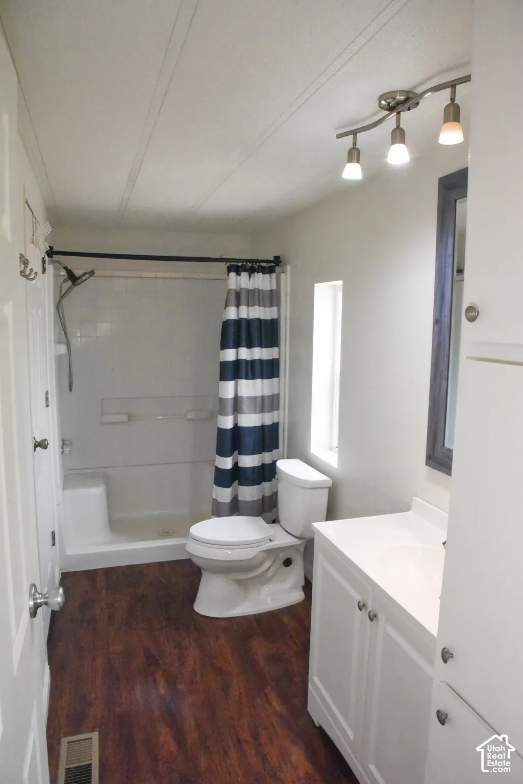Primary Bathroom featuring a white vanity with integrated sink, wood-finish flooring, and a white shower stall with a built-in bench