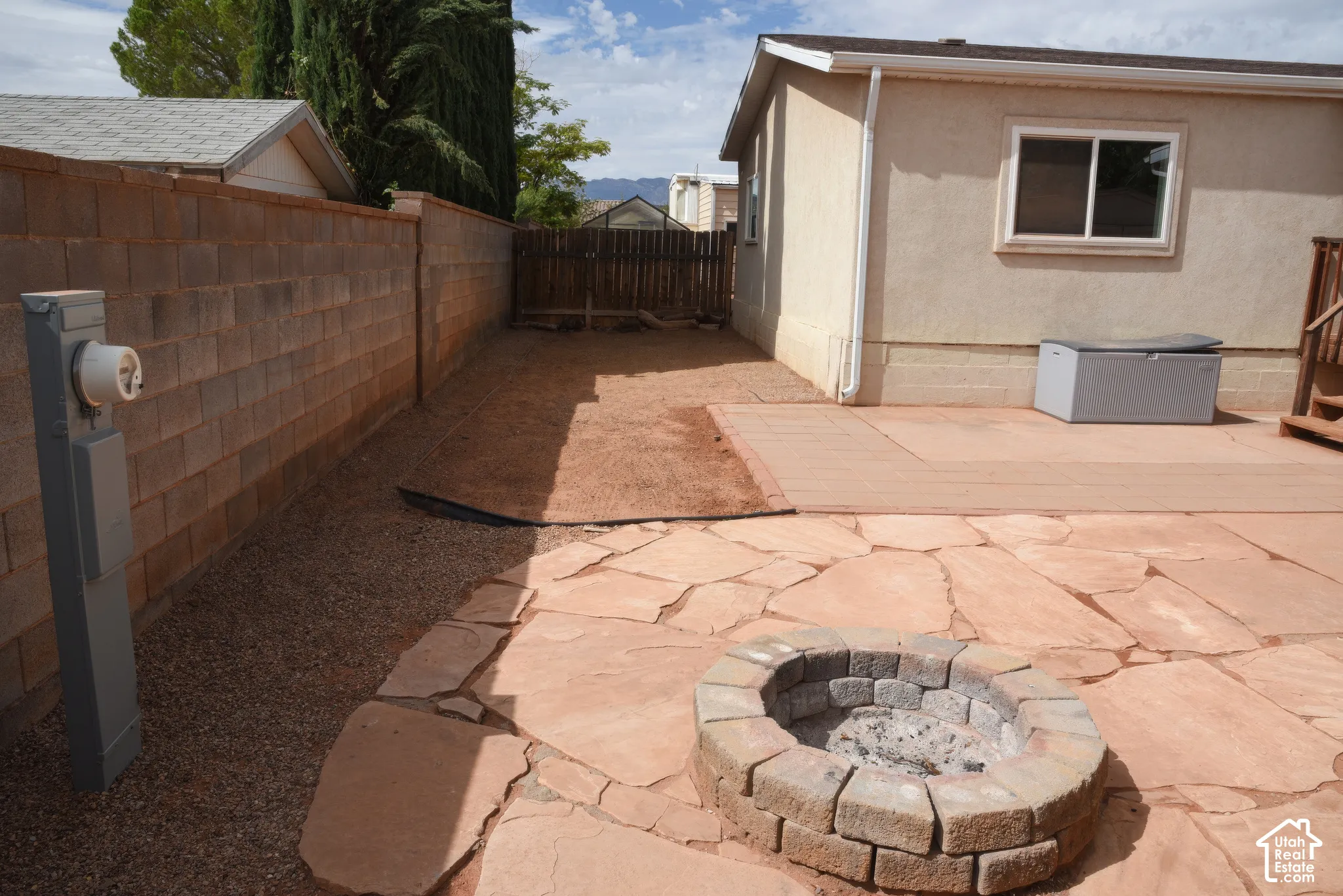 Stone patio with an integrated block fire pit, bordered by gravel and a concrete block privacy fence