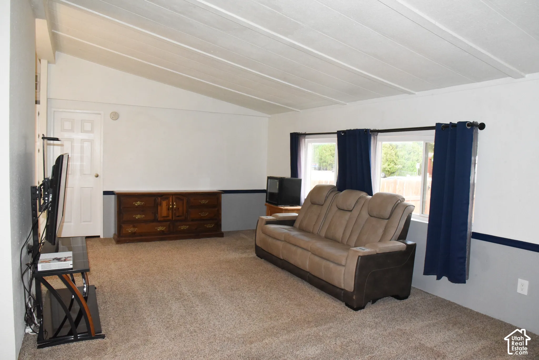 Vaulted ceilings with exposed beams, light neutral wall color, carpeted flooring, and multiple windows