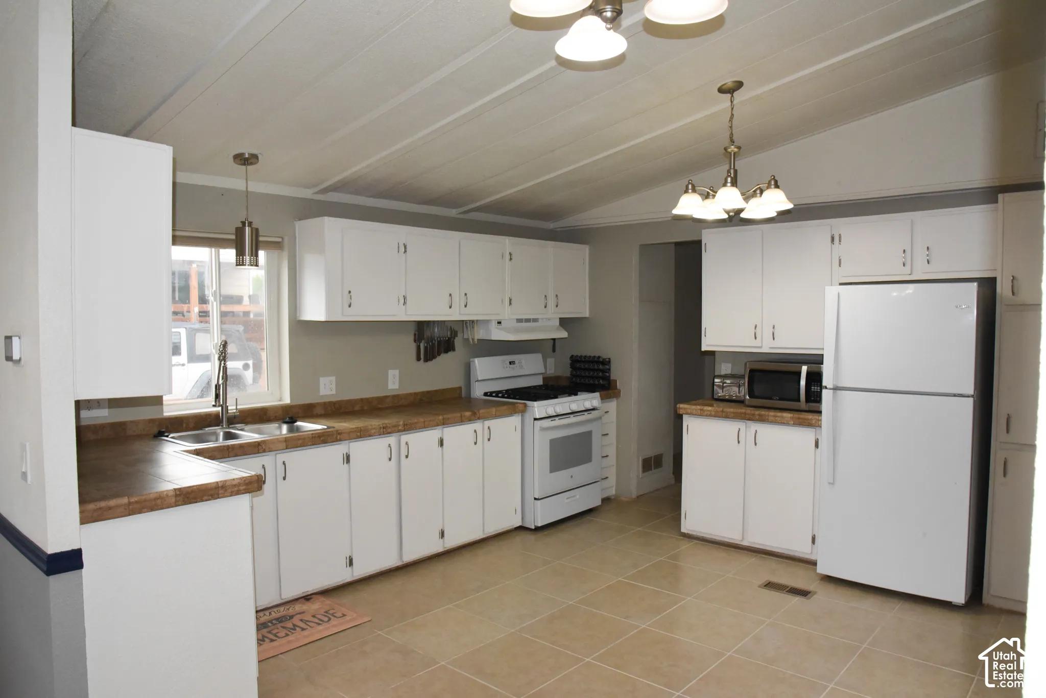 White cabinetry with brushed nickel hardware, laminate countertops, tile flooring, and a stainless steel double basin sink