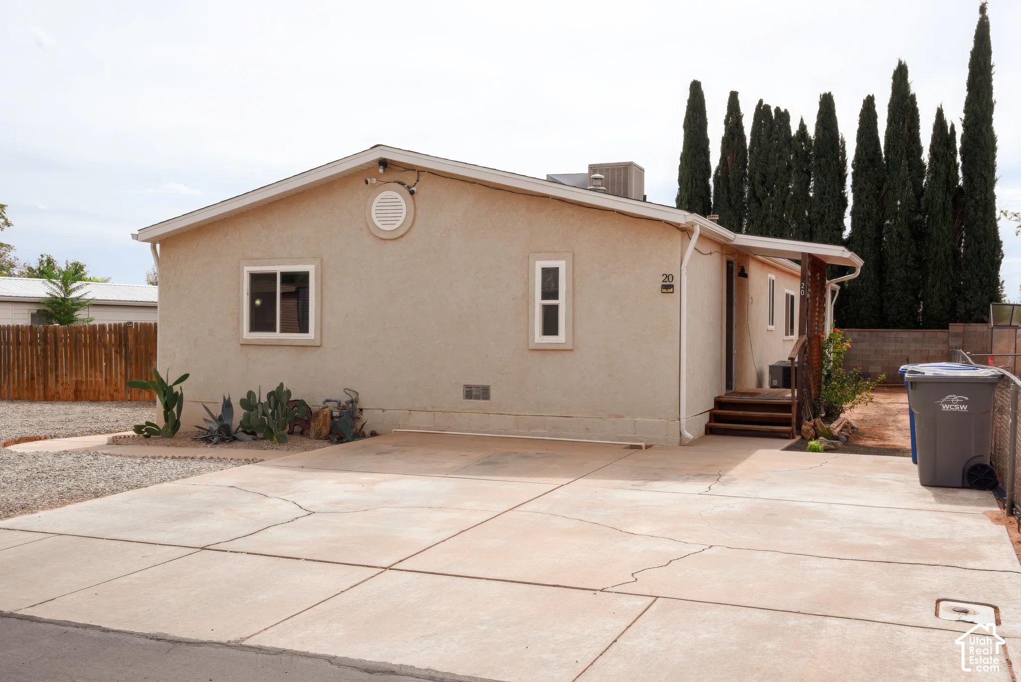 Parking Stucco exterior with a spacious concrete driveway and mature cypress trees providing privacy screening
